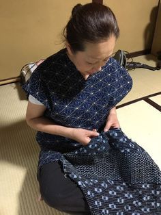 a woman is sitting on the floor with a piece of cloth in her hand and sewing