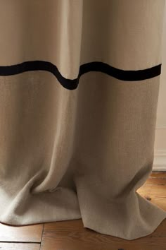 a close up view of a curtain with black stripes on the bottom and side, in front of a wooden floor