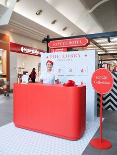 a woman standing behind a red counter in a store with a sign that says the lobby