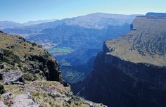 a man standing on the edge of a cliff looking out over a valley and mountains