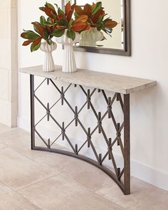 two vases with flowers sit on a console table in front of a wall mirror