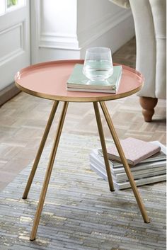 a pink table with books on it and a glass vase sitting on top of the table