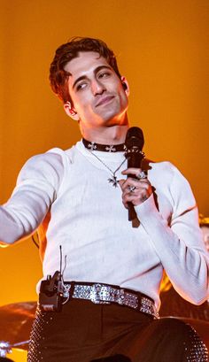 a man holding a microphone in his right hand and wearing a white shirt with sequins on it