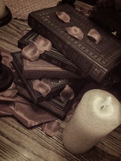 a stack of books sitting on top of a wooden table next to a lit candle