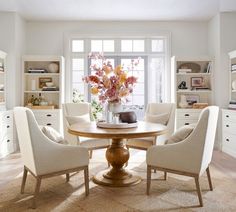 a table with four chairs around it in front of a window and some bookshelves