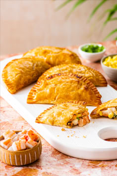 several different types of pastries on a cutting board next to bowls of salads