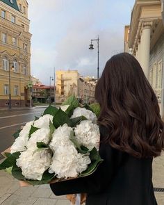 a woman walking down the street holding a bouquet of white flowers in front of her