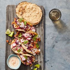 three tacos with toppings on a wooden board next to a small bowl of dipping sauce