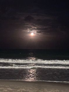 the moon is setting over the ocean with waves