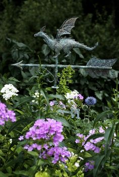 two metal dragon statues sitting on top of a pole in the middle of some flowers