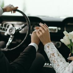 two people holding hands while sitting in a car with the driver's hand on the steering wheel