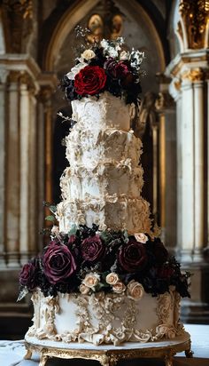 a three tiered wedding cake with red and white flowers on top sits in front of an ornate archway