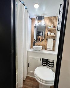 a white toilet sitting under a bathroom mirror next to a sink and wooden flooring