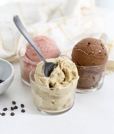 three scoops of ice cream sit in small glass bowls on a white tablecloth