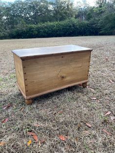 a wooden box sitting in the middle of a field with grass and trees behind it