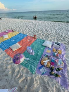 a blanket on the beach with food and drinks laid out for people to enjoy it