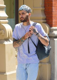 a man with grey hair and tattoos is carrying a black bag while walking down the street