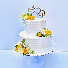 a three tiered white cake with yellow flowers on the bottom and gold initials on top