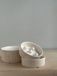 two white ceramic bowls sitting on top of a wooden table with the words stella king printed on them