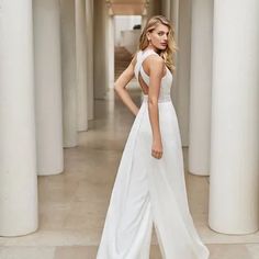 a woman in a white dress is standing near columns and looking at the camera with her hands on her hips