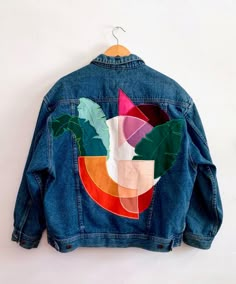 a denim jacket with an image of a bird and leaves on the back, hanging on a white wall