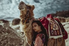 a woman standing next to a camel in the desert