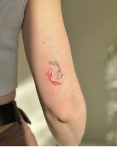 a woman's arm with a small red and white fish tattoo on the left arm