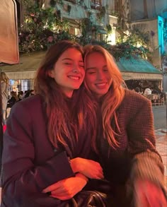 two young women sitting next to each other in front of a building with flowers on it