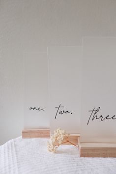 three cards with writing on them are sitting on a white tablecloth and one has a flower in front of it