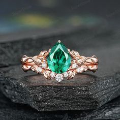 a ring with an emerald colored stone surrounded by white and rose gold accents on top of a rock