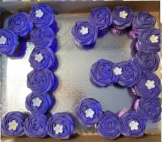 a box filled with purple cupcakes sitting on top of a metal pan covered in frosting