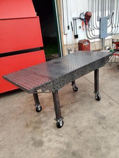 a metal table sitting on top of a cement floor in front of a red wall