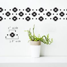 a potted plant sitting on top of a white table next to a wall with black and white designs