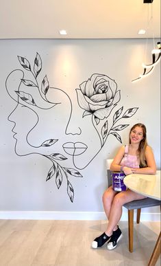 a woman sitting on a chair in front of a wall with flowers painted on it