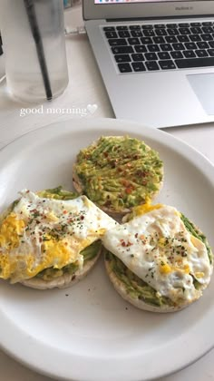 an open face sandwich on a white plate next to a laptop and cup of coffee