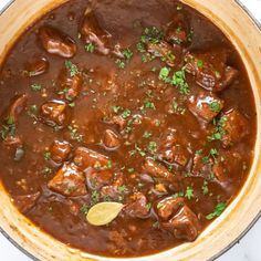 a pot filled with meat and sauce on top of a counter next to a wooden spoon