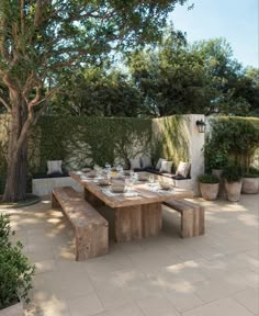 a wooden table sitting next to a tree on top of a stone floored patio