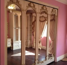 an ornately decorated mirror in the corner of a room with pink walls and wood floors