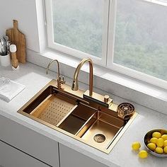 a kitchen sink sitting under a window next to a bowl of lemons and a cutting board