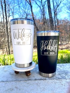 two personalized tumblers sitting on top of a cement slab in front of trees