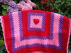 a crocheted blanket sitting in front of some flowers