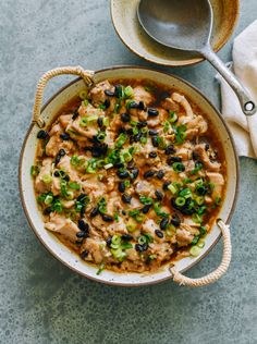 a bowl filled with chicken and black olives next to a measuring spoon on top of a table