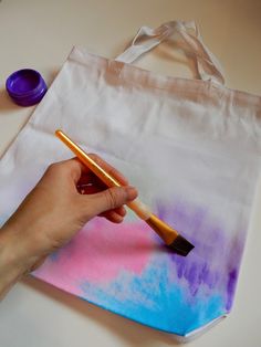 a person holding a paintbrush in front of a tote bag on a table