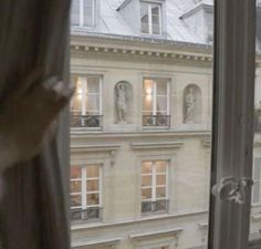 an open window looking out onto a building with statues on the windowsill and buildings in the background