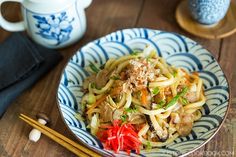 a blue and white bowl filled with food next to chopsticks on top of a wooden table