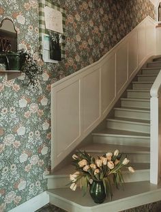 a vase filled with flowers sitting on top of a wooden table next to a stair case