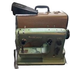 an old green sewing machine sitting next to a suitcase