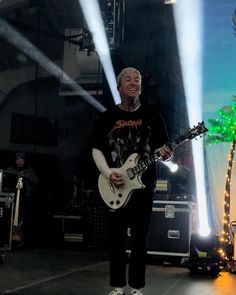 a man standing on top of a stage with a guitar in his hand and lights behind him