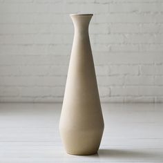 a white vase sitting on top of a table next to a brick wall and floor