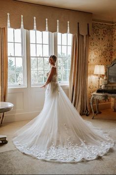 a woman standing in front of a window wearing a wedding dress